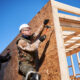 Carpenters hammering nail into OSB panel on the wall of a house.