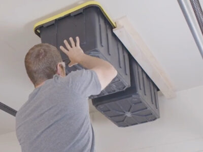 Man attaching garage storage bins to ceiling.