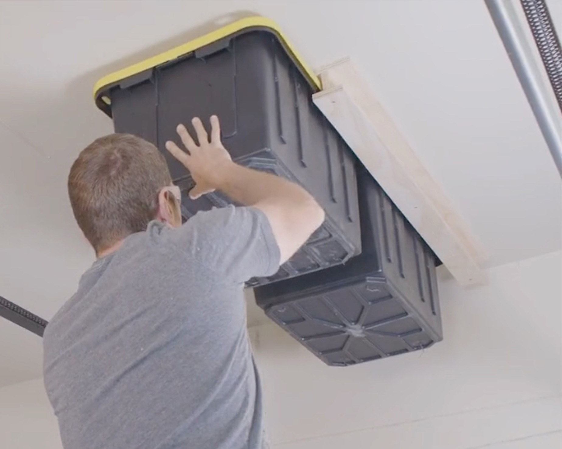 Man attaching garage storage bins to ceiling.