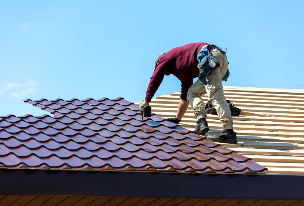 Workers install metal roofing on the wooden roof of a house. 